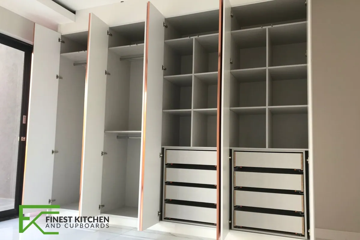 A white FKC built-in walk-in wardrobe with open shelving, hanging rails and a bank of drawers.