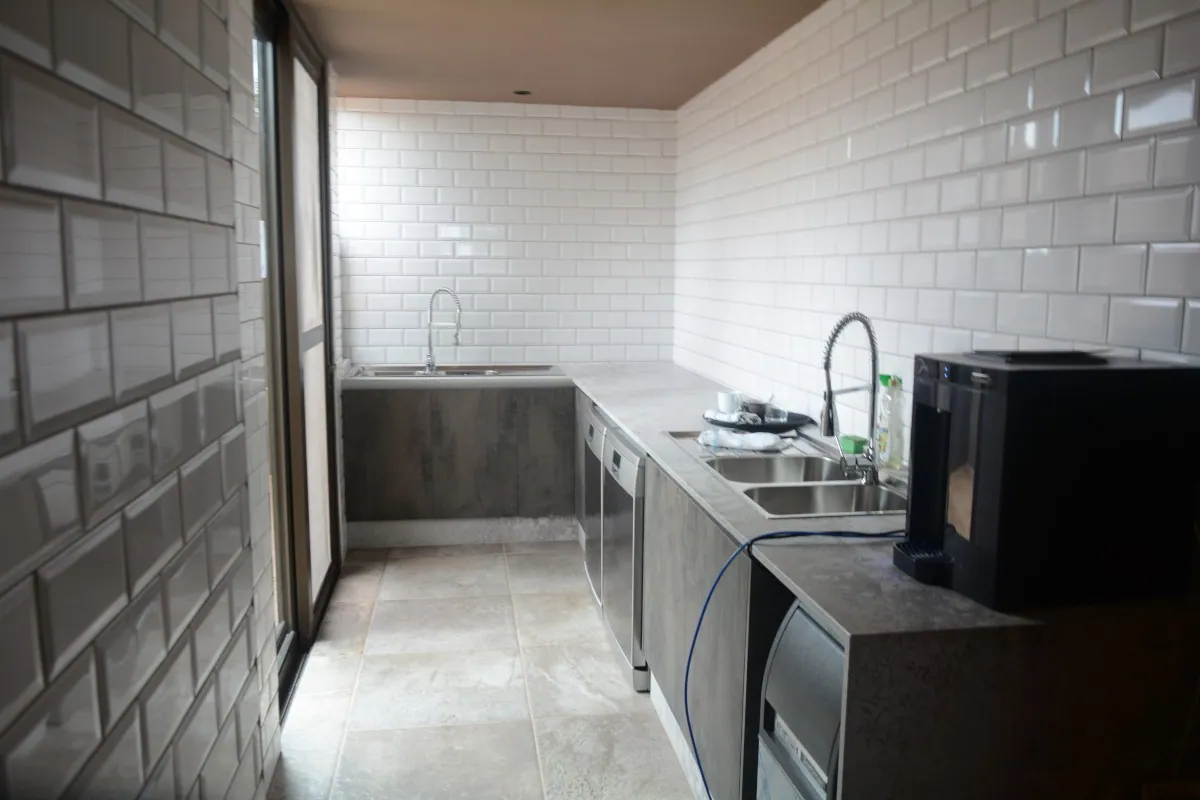 A narrow FKC scullery with white brick-tiled walls, a dark worktop and fitted base units.