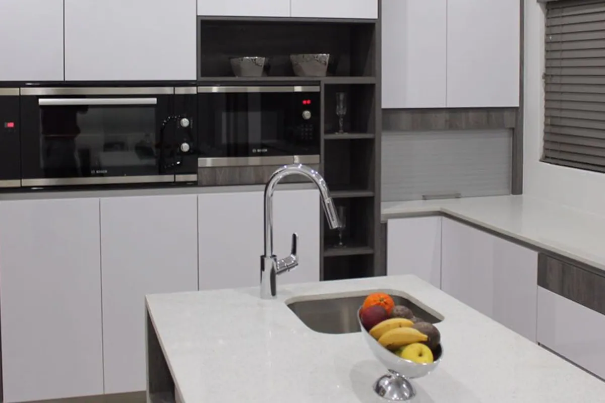 The sink run, with white gloss units, a black oven stack and a dark timber accent panel.