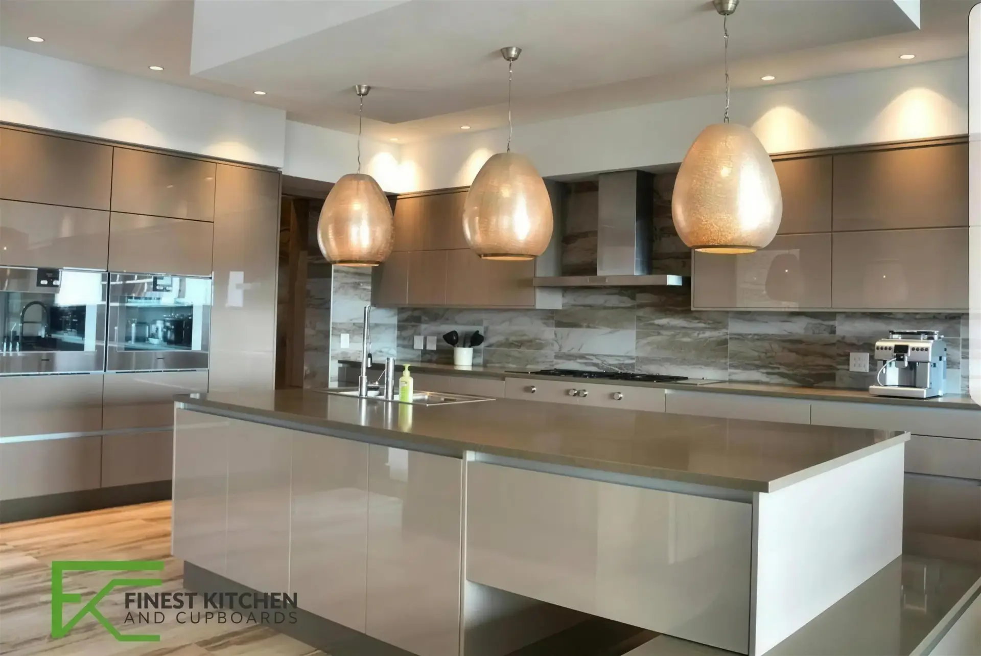 An FKC kitchen with a marble island lit by three copper pendant lights, warm wood wall units and a stone splashback.