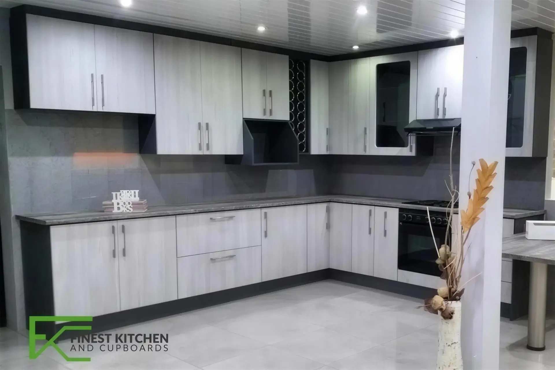 An L-shaped FKC kitchen in light timber and white, with a black oven stack built into a full-height run.