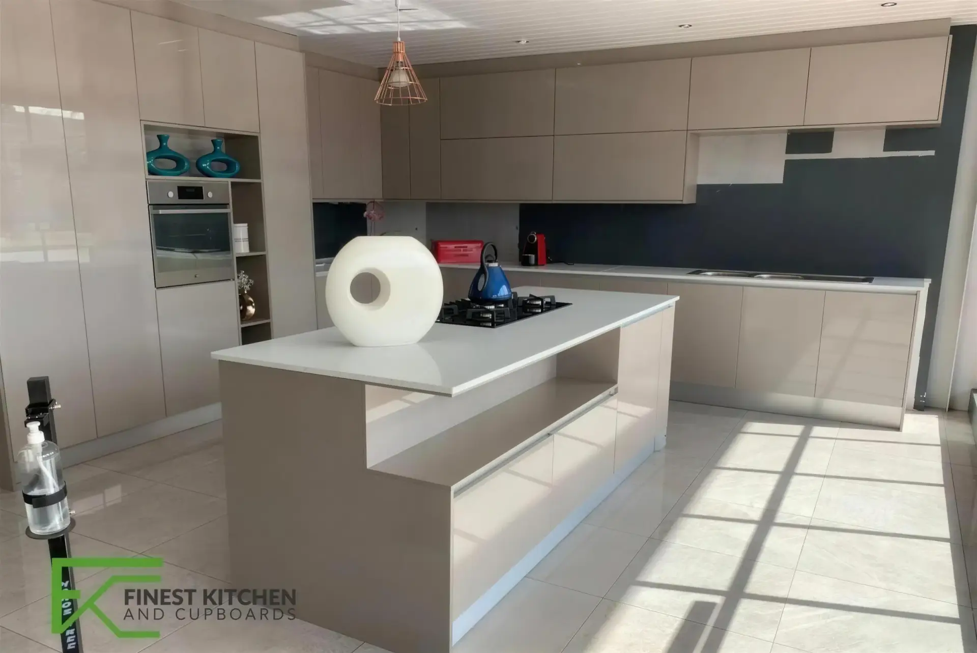 A cream FKC kitchen with a white-topped island, a single copper pendant light and a deep blue splashback.