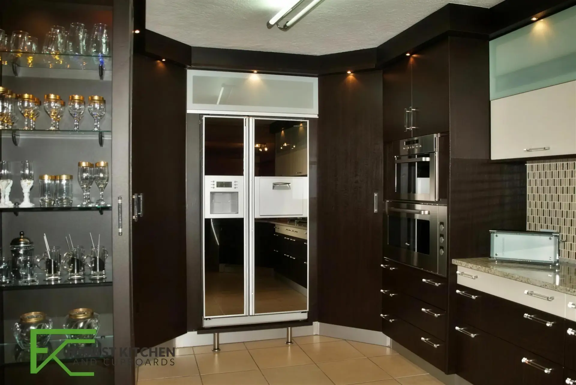 A dark timber FKC kitchen with a glass-fronted glassware display cabinet, integrated fridge and mosaic tiled splashback.