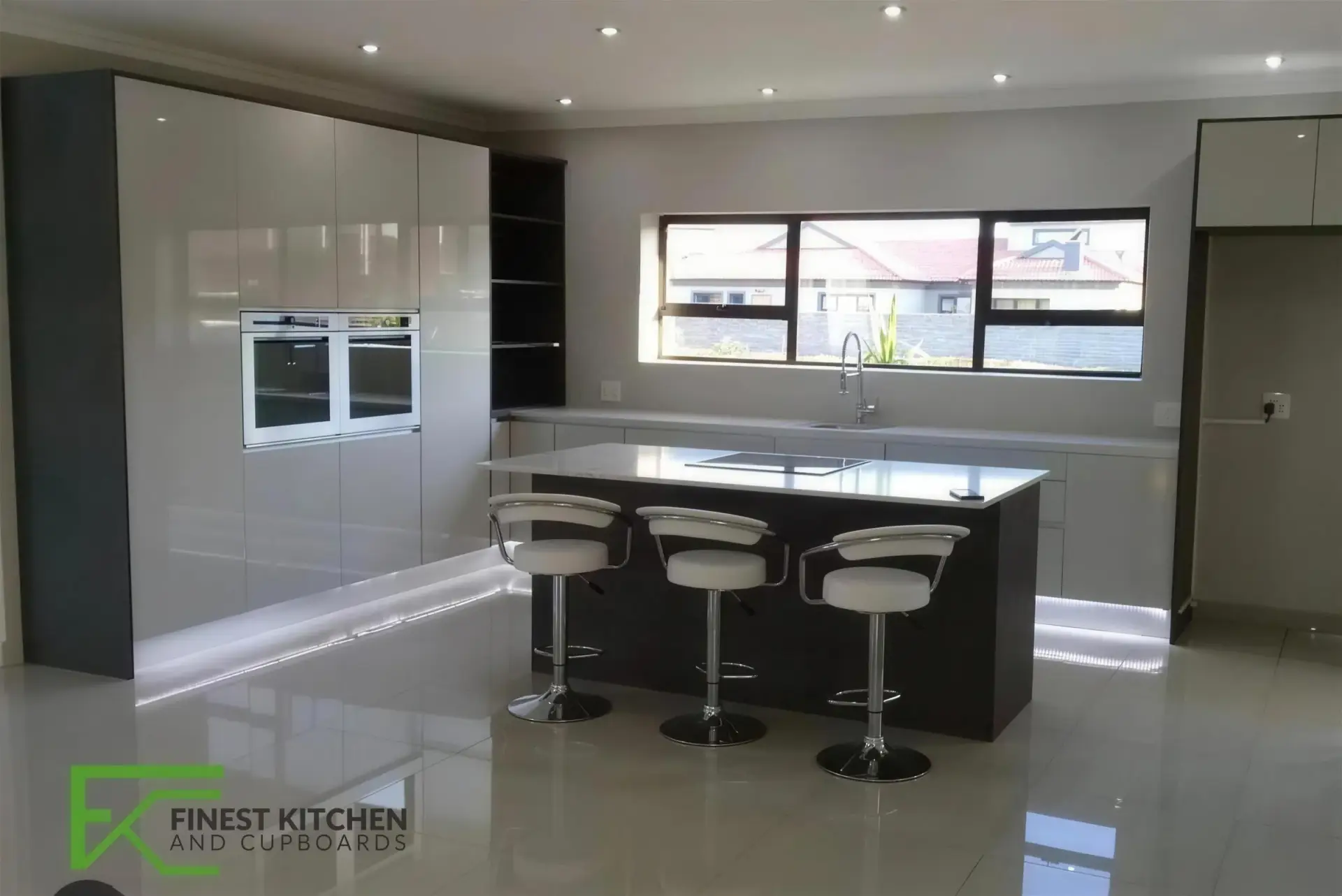 A grey gloss FKC kitchen with a breakfast bar, black bar stools and a run of windows behind.