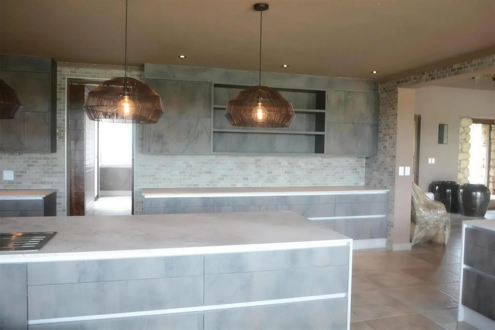 A finished FKC kitchen with a marble-topped island and copper pendant lights in an open-plan home.