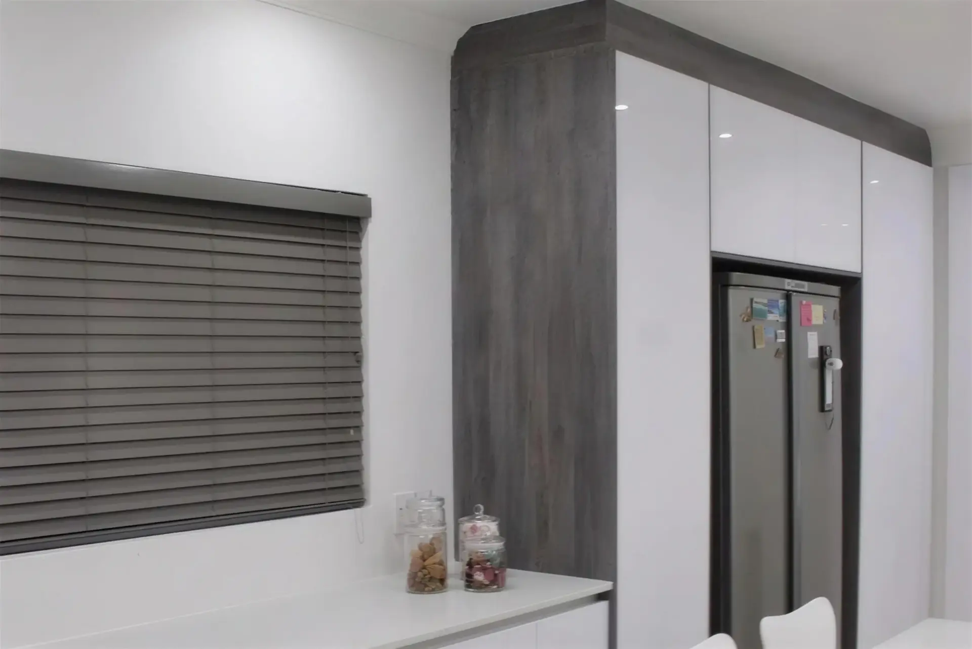 Kitchen Units 03: A white gloss kitchen with a black oven stack, dark timber shelving and an island with seating.