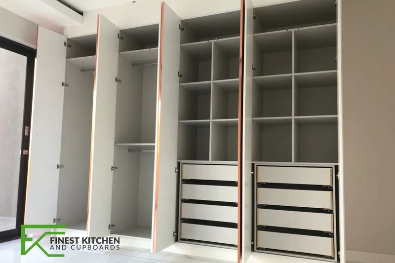 A white FKC built-in walk-in wardrobe with open shelving and drawers.