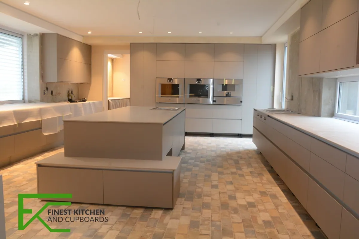 A bright FKC kitchen with a large white island, taupe base units and a wood-look tiled floor running into the living area.