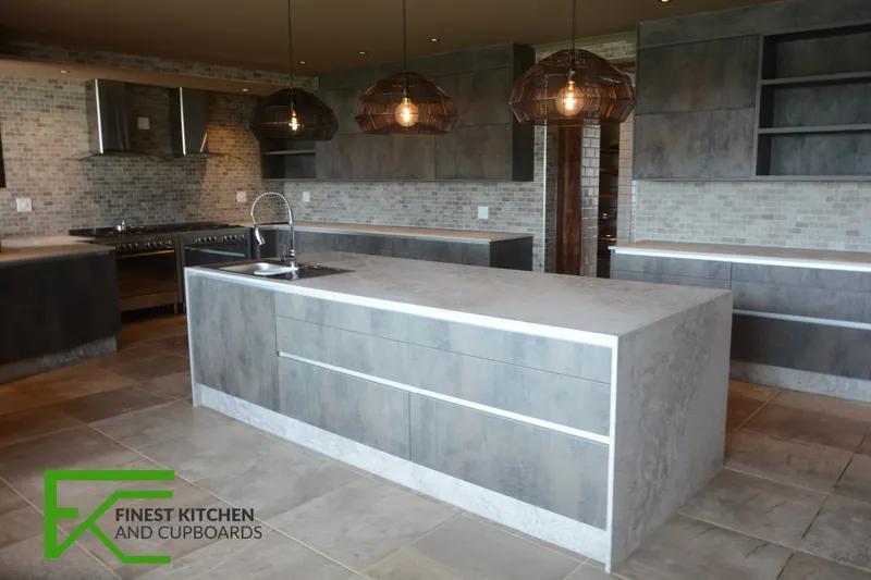 An FKC kitchen in stone and dark timber with a marble island, copper pendant lights and a textured stone splashback.