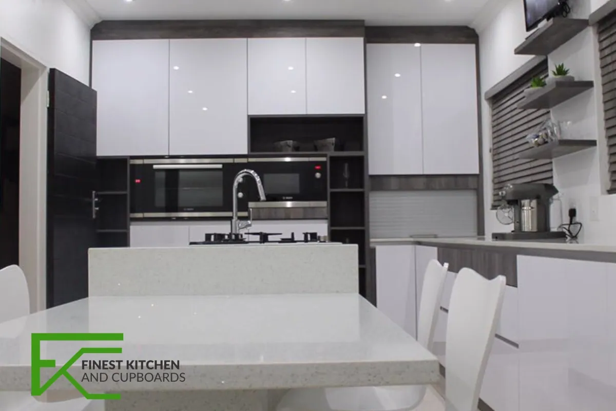 A white gloss FKC kitchen with a black oven stack, dark timber open shelving and an island with white bar chairs.