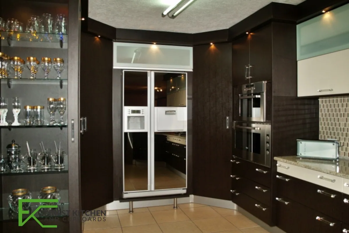 A dark timber FKC kitchen with a glass-fronted glassware display cabinet, integrated fridge and mosaic tiled splashback.