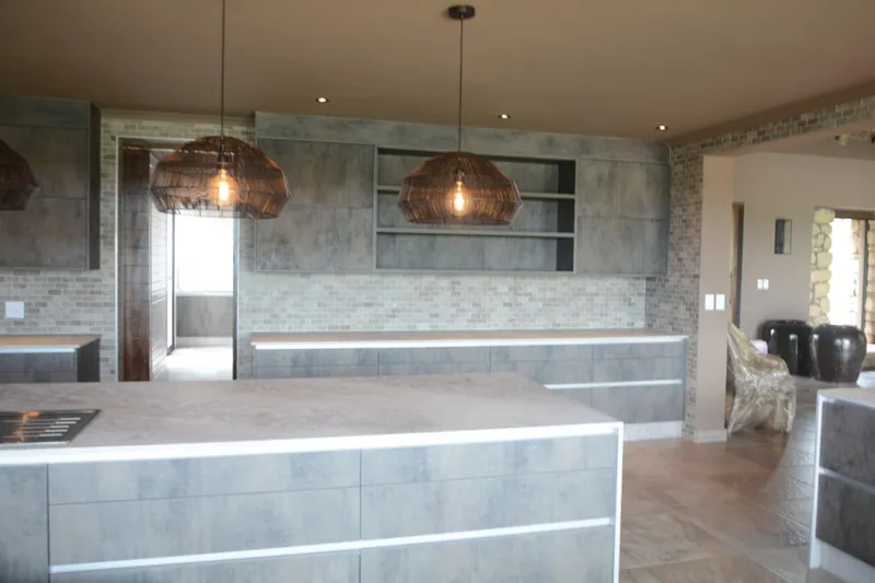 A marble-topped island kitchen with copper pendants, built into an open-plan living space by FKC Kitchens.