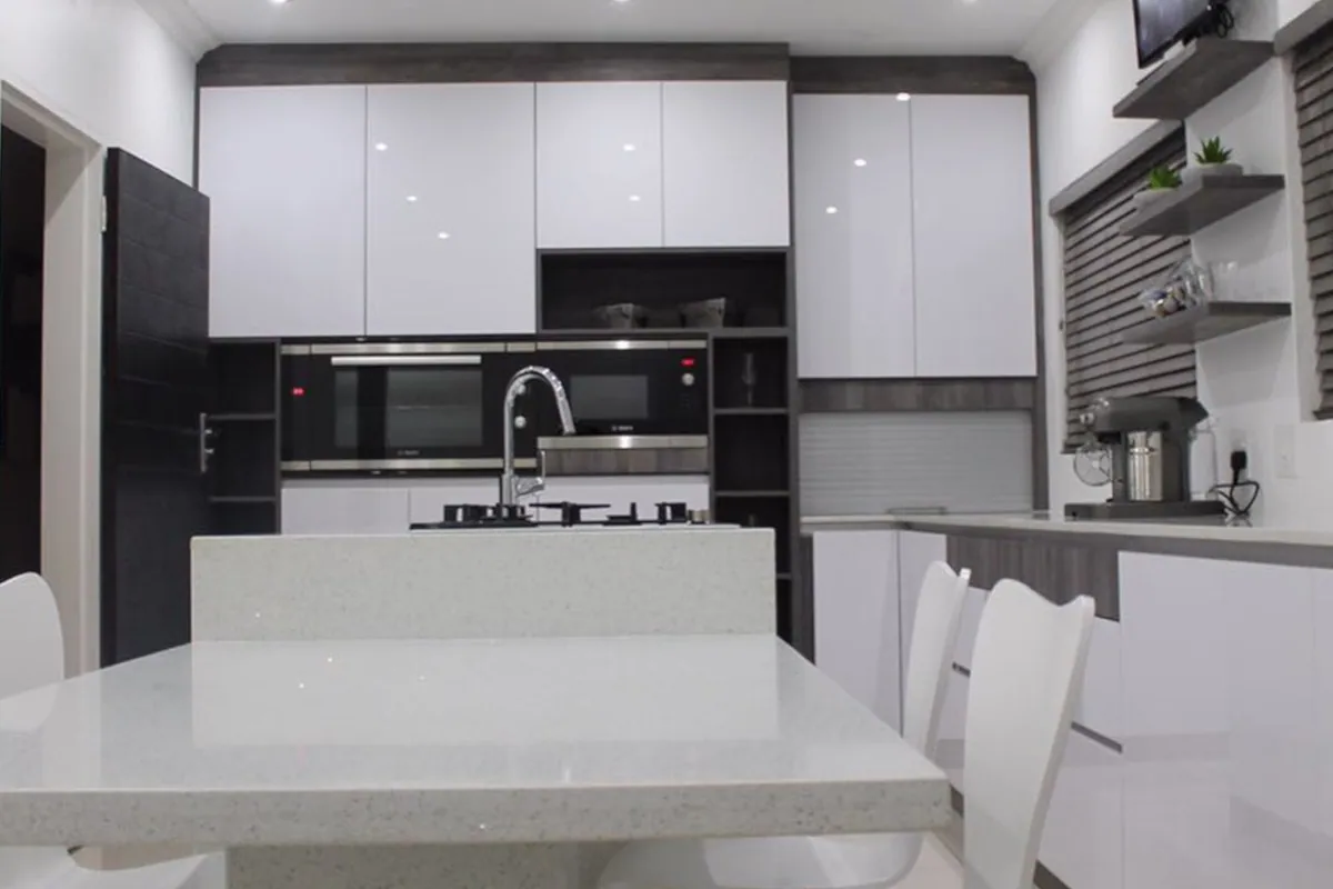 Kitchen Units 03: A white gloss kitchen with a black oven stack, dark timber shelving and an island with seating.