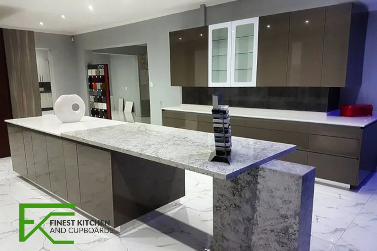 A dark grey FKC kitchen with a marble waterfall island, glass-fronted display cabinets and blue accent lighting.
