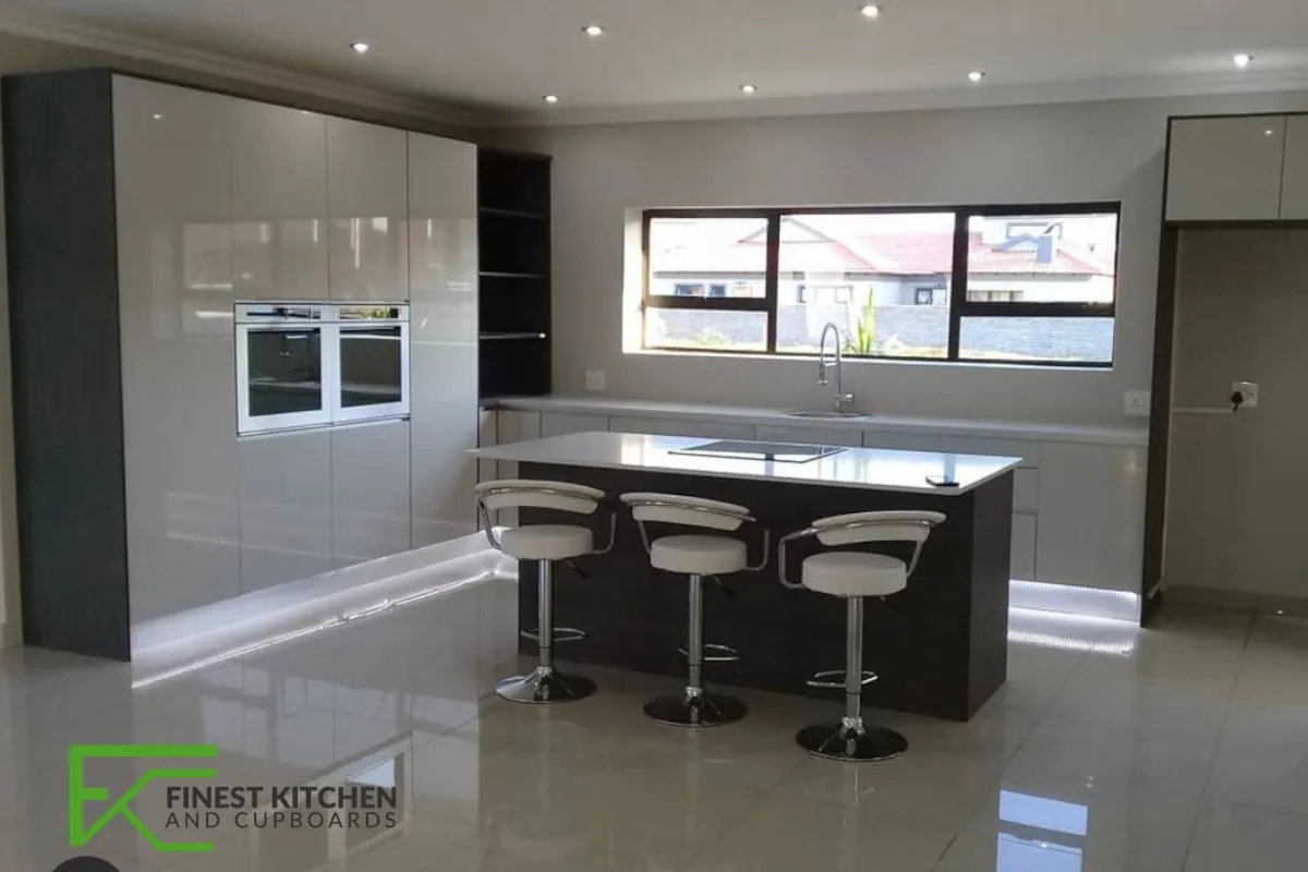 A grey gloss FKC kitchen with a breakfast bar, black bar stools and a run of windows behind.